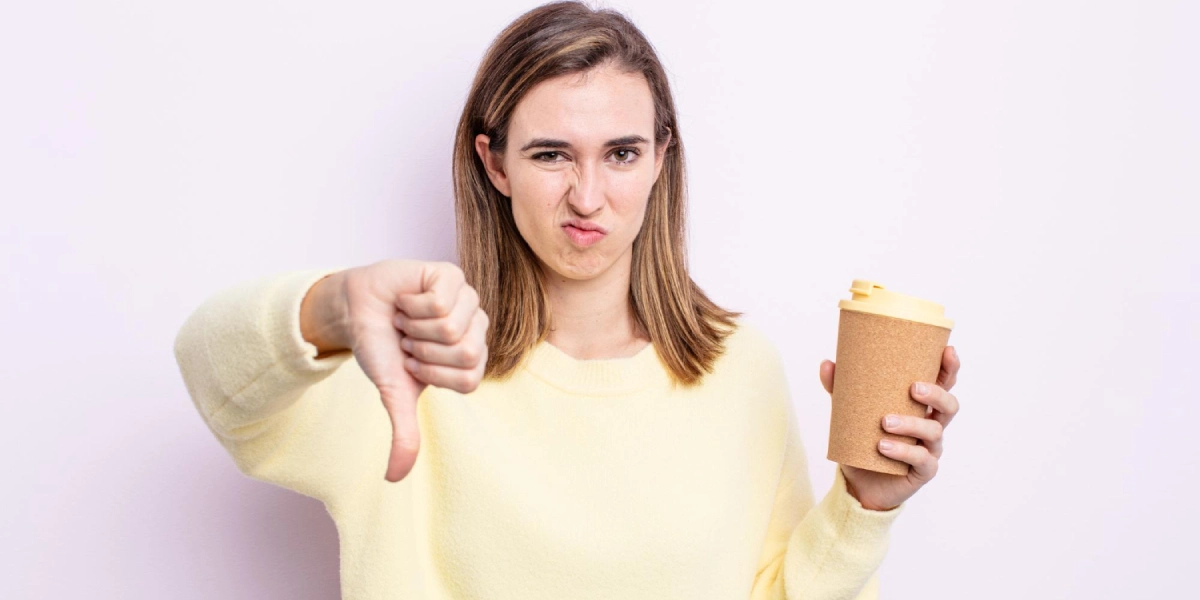 Kobieta z kawą w ręku pokazuje kciuk w dół